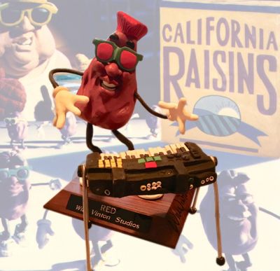 Red Raisin Puppet
Meet the Raisins! is a 1988 claymation television special directed by Will Vinton, featuring the advertising characters The California Raisins. It was the Raisins' second appearance in a primetime special and their first dedicated feature. Meet the Raisins! spoofs musical documentaries with its use of anthropomorphic produce characters. Through its historical perspective, the special also provided an opportunity to elaborate on the personalities and introduce names of the simple yet popular characters. It follows the California Raisins' humble beginnings, rise to musical success, fall from stardom, and eventual comeback. This is the screen used puppet and piano from Vinton Studios of the musician raisin known as Red.
Keywords: Red Raisin Puppet